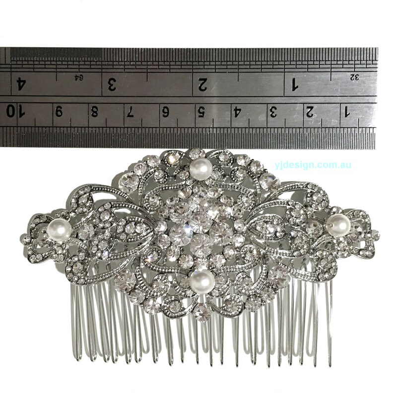 May include: Silver hair comb with a large, ornate design featuring clear rhinestones and faux pearls. The comb is approximately 4 inches wide.