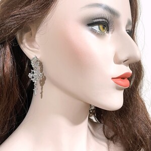 May include: Silver dangle earrings with a floral design and clear rhinestones.