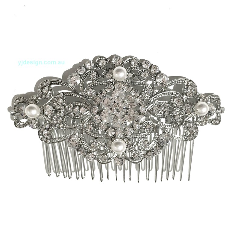 May include: Silver hair comb with a large, ornate design featuring clear rhinestones and faux pearls. The comb has a wide, flat base with a row of teeth.