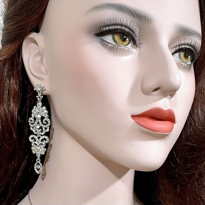 May include: A pair of silver dangle earrings with a crystal design. The earrings are long and feature a teardrop-shaped crystal at the bottom.