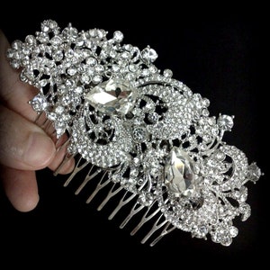 May include: A silver hair comb with a large, ornate design featuring clear rhinestones and two large teardrop-shaped crystals.