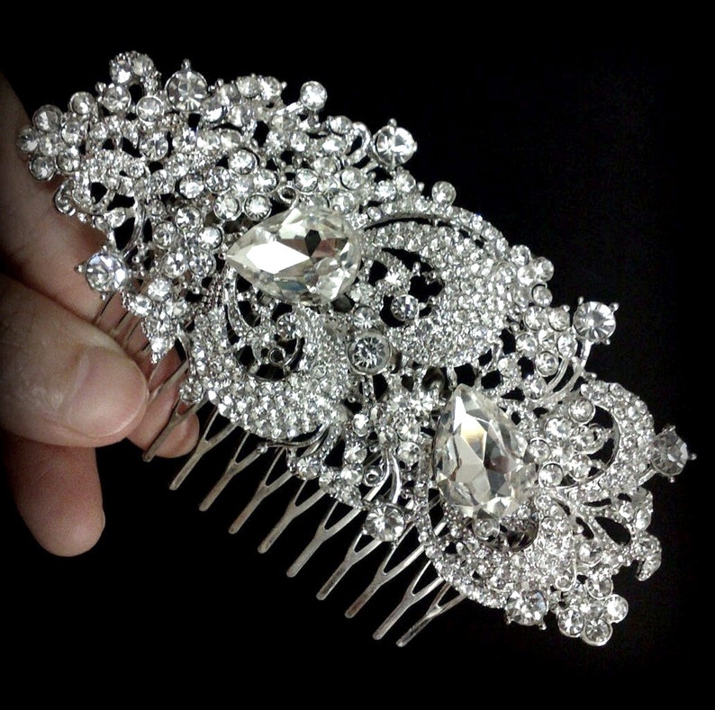 May include: A silver hair comb with a large, ornate design featuring clear rhinestones and two large teardrop-shaped crystals.