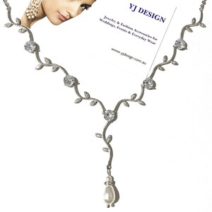 Op de afbeelding: Zilveren ketting met een parel hanger en heldere kristallen accenten. De ketting heeft een delicaat rankontwerp met bladeren en kleine ronde kristallen. De hanger is een enkele parel druppel.