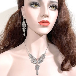 May include: A silver necklace and earrings set with a delicate, intricate design featuring a cascade of sparkling rhinestones.