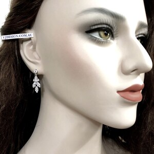 May include: A dangling earring with a cluster of clear, sparkling crystals. The earring features a small, round crystal at the top, with a design of marquise and round-cut crystals cascading downwards. The earring is shown on a mannequin.