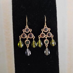 May include: A pair of gold dangle earrings with green and blue gemstone accents. The earrings feature a teardrop shape with a cluster of smaller gemstones.