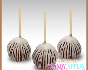 May include: Three white chocolate covered caramel apples with a white drizzle on a stick. The apples are arranged in a row on a white surface. The text "WHOLESALE CANDY APPLES" is visible in the bottom right corner of the image.