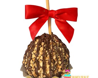 May include: A chocolate-covered apple with chopped peanuts and a drizzle of chocolate. The apple is on a gold paper doily and has a red ribbon tied around the wooden stick.