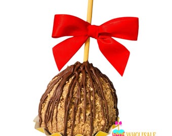 May include: A chocolate-covered caramel apple with a crunchy topping, decorated with a red bow and a wooden stick. The apple is sitting on a yellow paper wrapper.