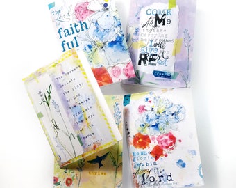 May include: Five art cards with watercolour floral designs and inspirational text. The cards feature various colours, including blue, pink, and yellow, with handwritten script and floral illustrations. The text includes phrases like "The Lord is faithful" and "Come to me."