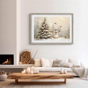May include: A framed winter landscape painting featuring a snow-covered Christmas tree and a snowman with a black hat and red scarf. The artwork has a light gray wooden frame and depicts a snowy scene with birds in the sky.