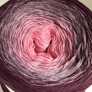 Könnte beinhalten: Eine Knäuel ombre Garn in den Farben Rosa, Lila und Burgunderrot. Das Garn ist zu einer Kugel gewickelt und bereit zum Stricken oder Häkeln.