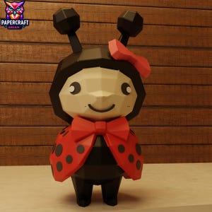 May include: A papercraft ladybug figure with a black body, red wings with black spots, and a red bow. The figure has a smiling face and is set against a wooden background. The logo "PAPERCRAFT DREAM" is in the upper left corner.