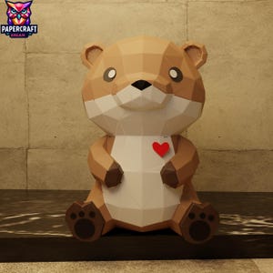 Può includere: Una lontra di carta marrone e bianca con un cuore rosso sul petto. La lontra ha un design geometrico ed è seduta. Il logo Papercraft Dream si trova nell'angolo in alto a sinistra.