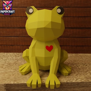 May include: A yellow geometric papercraft frog with a red heart on its chest. The frog has large, round eyes. The Papercraft Dream logo is in the upper left corner. The frog is sitting on a surface.