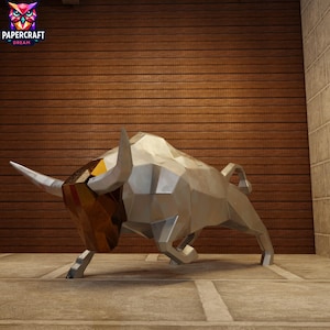 May include: A silver geometric sculpture of a bull with a brown and gold head. The sculpture is standing on a concrete surface in front of a wooden wall. The Papercraft Dream logo is in the upper left corner.