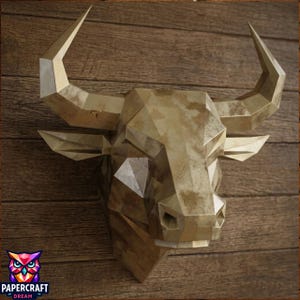 May include: A geometric bull head wall sculpture featuring a metallic gold finish with a weathered, mottled texture. The design is composed of sharp, angular facets forming the snout, ears, and two large, pointed horns extending outward.
