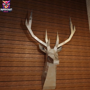 May include: A geometric papercraft deer head sculpture mounted on a wooden wall. The sculpture is primarily silver and beige, with sharp angles and a modern aesthetic. The wall has horizontal wooden planks.