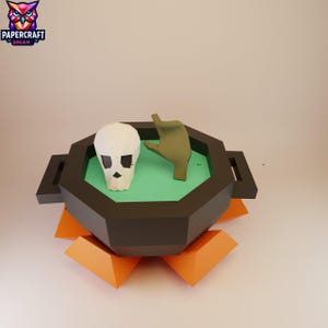 May include: A 3D papercraft model featuring a skull and a hand inside a black octagon-shaped container with a green interior. The container sits atop an orange geometric base. The Papercraft Dream logo is in the upper left corner.