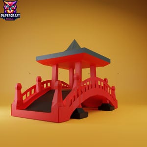 Könnte beinhalten: Eine rote Papierbrücke mit einem Dach im Pagodenstil. Die Brücke hat ein geschwungenes Design mit dekorativen Geländern. Das Dach ist grau und die Struktur befindet sich vor einem gelben Hintergrund. Das Papercraft Dream-Logo befindet sich in der oberen linken Ecke.