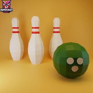 Puede incluir: Una representación 3D de un juego de bolos. Tres bolos blancos con rayas rojas están detrás de una bola de bolos verde con tres agujeros blancos. El fondo es de color amarillo-naranja. El logotipo "PAPERCRAFT DREAM" está en la esquina superior izquierda.