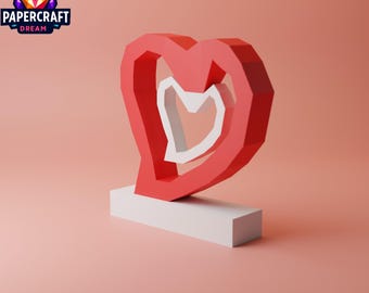 May include: A red papercraft heart sculpture with a white heart inside, standing on a white base. The sculpture is on a pink background.