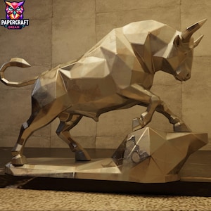 Può includere: Una scultura di toro in metallo dorato dal design geometrico sfaccettato. Il toro è raffigurato in posizione di carica con la testa abbassata e le corna rivolte in avanti, poggiato su una base angolare coordinata dalla superficie liscia.