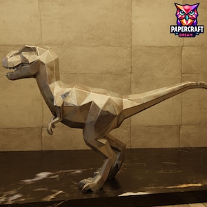 Może przedstawiać: Metaliczna srebrna rzeźba dinozaura T-Rex o geometrycznym, fasetowanym designie typu low-poly. Figurka przedstawiona jest z profilu, posiada długi ogon, małe ramiona oraz otwarty pysk z widocznymi zębami, wykończona odblaskową powierzchnią.