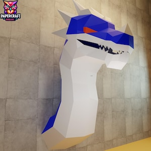 Może przedstawiać: Duża, geometryczna papierowa głowa smoka zamontowana na ścianie. Smok ma białe ciało, niebieską głowę i akcenty oraz pomarańczowe oko. Logo Papercraft Dream znajduje się w lewym górnym rogu.