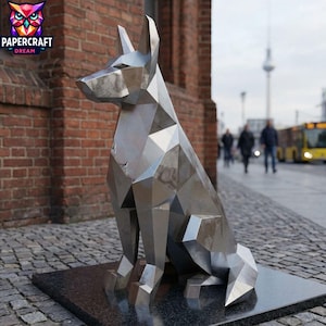 May include: A silver geometric dog sculpture in a seated pose, set on a dark rectangular base. The background features a brick building, a pavement, and pedestrians. The sculpture is made of metal.