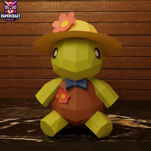 Può includere: Una figura di tartaruga di carta con un cappello giallo con un fiore rosa, un gilet marrone e un papillon blu. La tartaruga ha un design geometrico ed è ambientata su uno sfondo di legno. Il logo Papercraft Dream è in alto a sinistra.