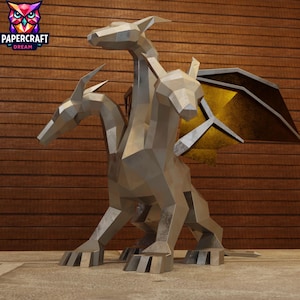 Puede incluir: Una escultura metálica y geométrica de un dragón de tres cabezas con grandes alas. La escultura está colocada sobre un fondo de madera, con el logotipo de Papercraft Dream en la esquina superior izquierda.