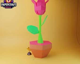 May include: A pink papercraft tulip with green leaves in a brown pot. The flower is standing on a yellow surface.