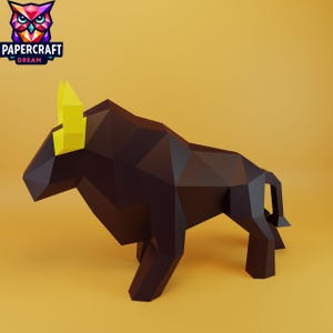 Könnte beinhalten: Ein brauner Papier-Bulle mit gelben Hörnern steht auf einer gelben Oberfläche. Der Bulle besteht aus geometrischen Formen. Das Papercraft Dream-Logo mit einer bunten Eule befindet sich in der oberen linken Ecke.