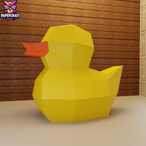 May include: A large, geometric yellow duck with an orange beak. The duck is made of multiple flat planes, giving it a polygonal appearance. The background is a wooden wall. The logo "PAPERCRAFT DREAM" is in the upper left corner.