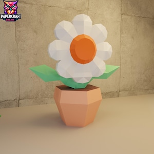Puede incluir: Una flor de papel en una maceta. La flor tiene pétalos blancos y un centro naranja. Las hojas son verdes y la maceta es de color melocotón. El logotipo de Papercraft Dream está en la esquina superior izquierda.