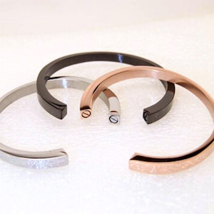 May include: Three metal bracelets in silver, rose gold, and black. Each bracelet has a simple, minimalist design with a small screw detail at the clasp.