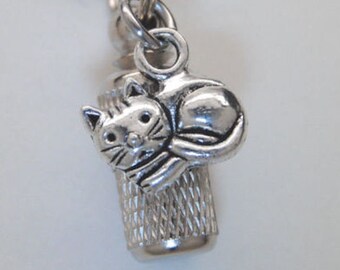 May include: Silver chain necklace with a small silver urn pendant featuring a cat charm. The urn has a textured surface.