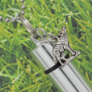 May include: Silver necklace with a small, detailed wolf charm attached to a silver cylinder pendant. The pendant has a black rubber band around it.