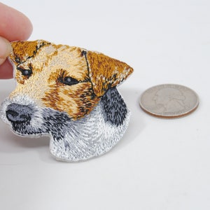 May include: Embroidered patch of a Jack Russell Terrier dog's head. The patch is white with brown and black markings. The dog is looking to the left. The patch is about the size of a US quarter.