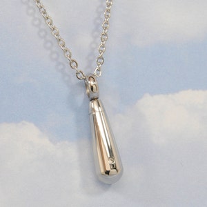 May include: A silver teardrop-shaped pendant necklace with a small diamond accent. The necklace is on a silver chain.