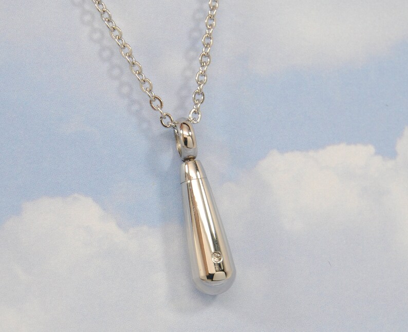 May include: A silver teardrop-shaped pendant necklace with a small diamond accent. The necklace is on a silver chain.