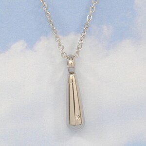 May include: A silver teardrop-shaped pendant necklace with a small diamond accent. The necklace is on a silver chain.