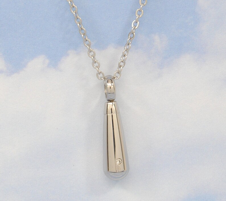 May include: A silver teardrop-shaped pendant necklace with a small diamond accent. The necklace is on a silver chain.