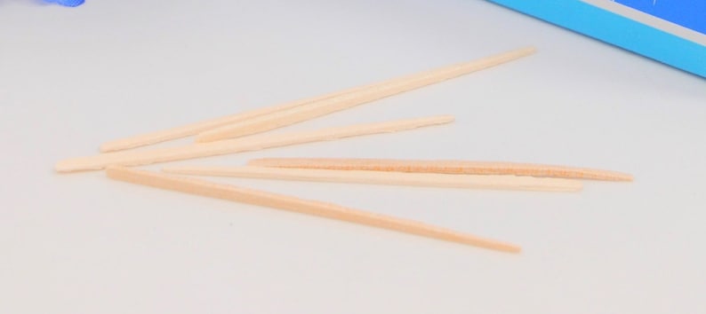 May include: A group of six wooden toothpicks arranged in a fan shape on a white surface.