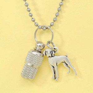 May include: Silver chain necklace with a silver dog charm and a silver cylinder charm. The dog charm is of a standing dog breed. The cylinder charm has a textured surface.
