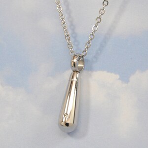 May include: A silver teardrop-shaped pendant necklace with a small, round opening at the top. The pendant is attached to a silver chain.