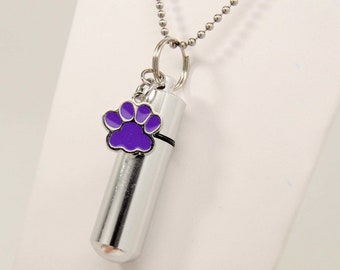 May include: Silver necklace with a small purple paw print charm and a silver cylinder pendant. The pendant is a cremation urn for holding ashes.