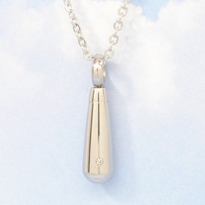 May include: A silver teardrop-shaped pendant necklace with a small diamond accent. The necklace is on a silver chain.