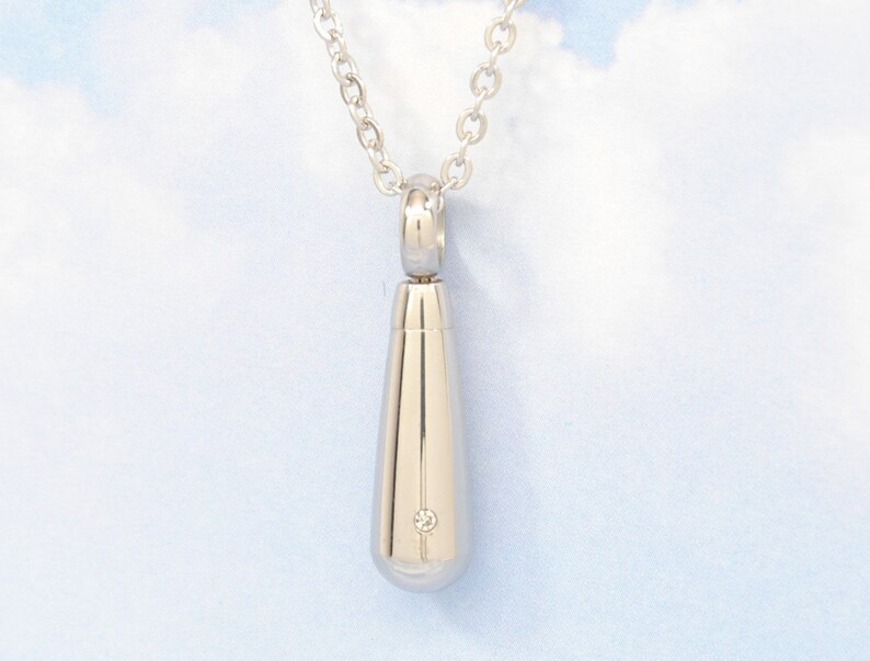 May include: A silver teardrop-shaped pendant necklace with a small diamond accent. The necklace is on a silver chain.
